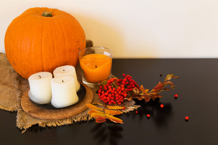 Autumn composition of rowan berries, pumpkins, candles and colorful leaves on the cloth of burlap on white and black backgroundの写真素材