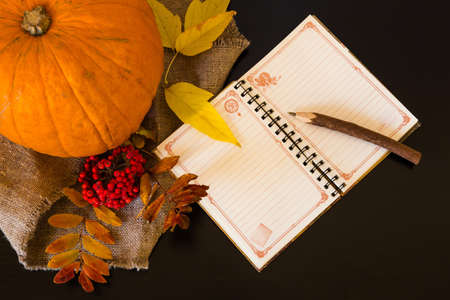 Autumn composition of notebook and pen among rowan berries, pumpkins, candles and colorful leaves on the cloth of burlap on black and white backgroundの写真素材
