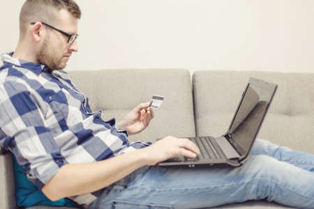 a man with a credit card for laptop in sofaの写真素材