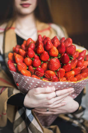 Bouquet of strawberries close-up in the hands of a girlの写真素材