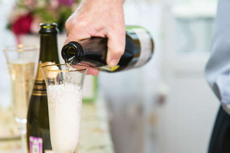 a mans hand pours champagne from a bottle into a glassの写真素材
