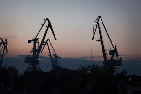 silhouettes of cranes on the extraction of river sand in a quarry against the backdrop of the sunsetの写真素材