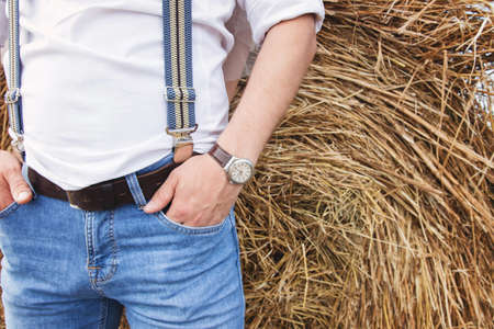 a man in blue jeans and a white shirt with suspenders in the background of a haystackの写真素材