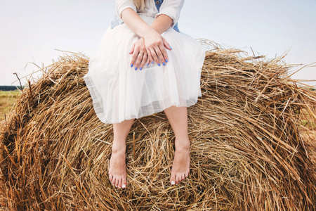 legs of a girl in a white dress and a blue denim jelly sitting on a haystackの写真素材