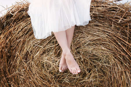 legs of a girl in a white dress and a blue denim jelly sitting on a haystackの写真素材