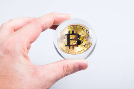 golden bitcoin in hand through magnifier close-up on white backgroundの写真素材