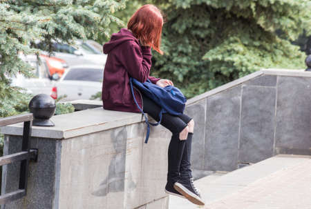 girl in ragged jeans sits in the city park and enjoys the phoneの写真素材