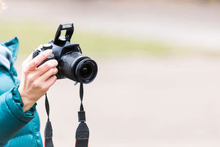 a female hand holds a professional digital SLR camera close-up on a blurred background.の写真素材