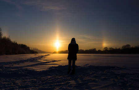 Female silhouette against the background of the setting sun and the natural atmospheric phenomenon of parhelion or the false sun.の写真素材