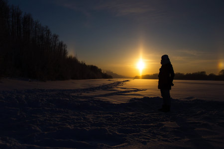 Female silhouette against the background of the setting sun and the natural atmospheric phenomenon of parhelion or the false sun.の写真素材