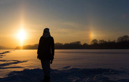 Female silhouette against the background of the setting sun and the natural atmospheric phenomenon of parhelion or the false sun.の写真素材