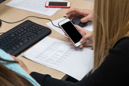 the girl is sitting at a desk by the computer among office supplies and is holding a phone in her hands. Work in the office or studyの写真素材