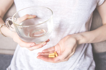 girl holding a glass of water and a handful of pillsの写真素材