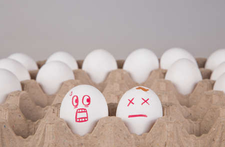concept. two eggs among the rest in the package. an egg with a smile of horror looks at the broken egg.の写真素材