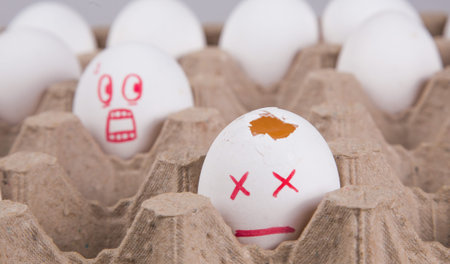 concept. two eggs among the rest in the package. an egg with a smile of horror looks at the broken...
