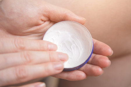 A female hand holds a jar of cream, for hands and face and puts it on the arm. women's beauty and...