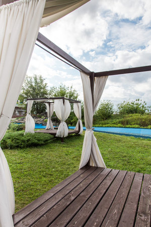 Summer wooden gazebo with a white cloth in the garden.の写真素材