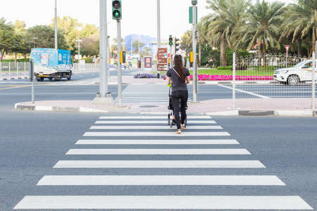 Dubai, UAE February 19, 2018: A young woman with a stroller crosses the road on a pedestrian crossing. back viewのeditorial素材