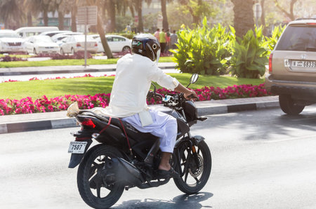 Dubai, UAE February 14, 2018: motorcyclist in national Arab clothing on a city road among cars