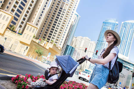 Dubai, UAE February 19, 2018: A young woman with a stroller crosses the road on a pedestrian crossing in a modern city against the backdrop of skyscrapersのeditorial素材