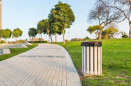 a trash bin in a public city park amidst a green lawn and treesの写真素材