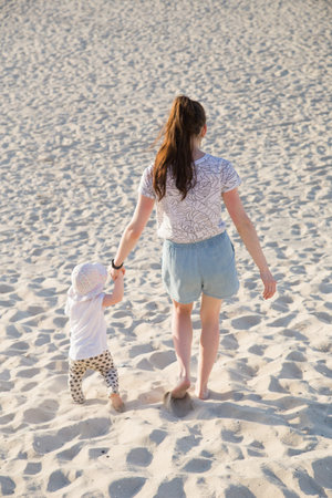 Mother teaching baby to walk on sand. summer fun at the beachの写真素材