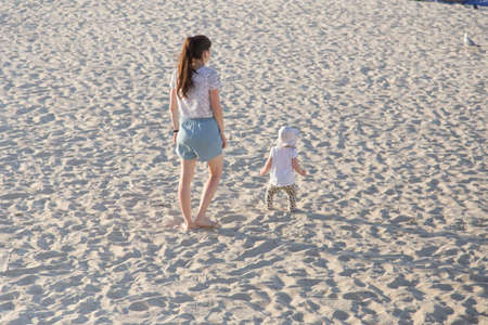 Mother teaching baby to walk on sand. summer fun at the beachの写真素材