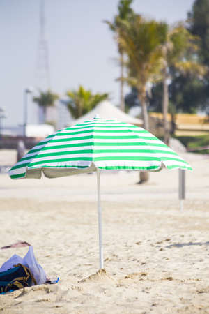 stripped beach umbrella with green and white stripes on the sandの写真素材