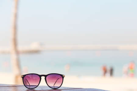 sunglasses with ultraviolet shade of glass on a wooden table on the background of the beach and the seaの写真素材