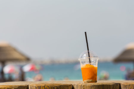 bright orange cold refreshing smoothie drink in a plastic cup with a black straw in the sand on a beach background on a hot sunny day. Travel conceptの写真素材