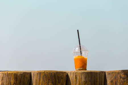 bright orange cold refreshing smoothie drink in a plastic cup with a black straw in the sand on a beach background on a hot sunny day. Travel conceptの写真素材