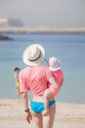 young beautiful mother holding a small daughter in her arms on a summer day at the beach. tropical family vacationの写真素材