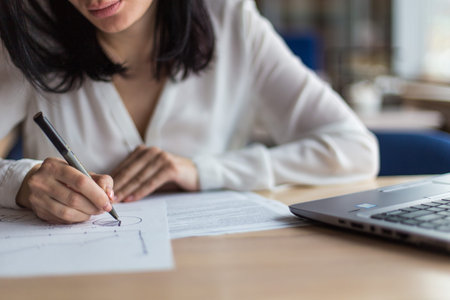 Brunette Business woman working behind laptop and with papers near window in cozy cafe atmosphere