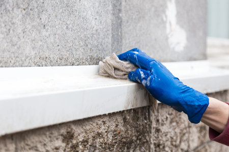 A young male cleaner in blue overalls washes building's facade, windows and store front. Cleaning Service close upの写真素材