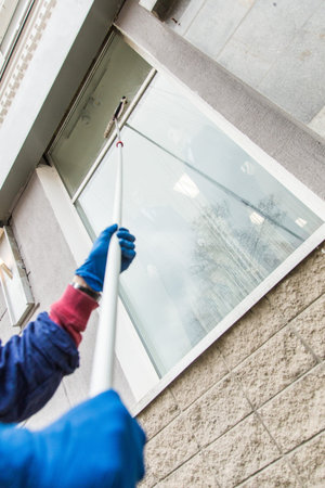 A young male cleaner in blue overalls washes building's facade, windows and store front. Cleaning Service close upの写真素材