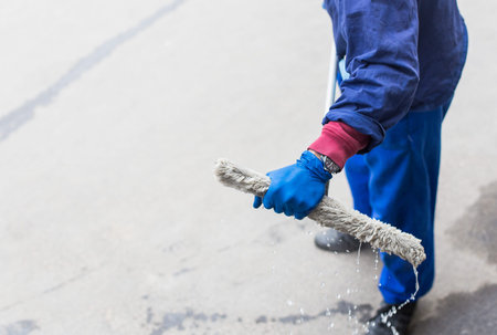 A young male cleaner in blue overalls washes building's facade, windows and store front. Cleaning Service close upの写真素材