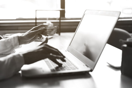 A young business woman with glasses is sitting in a cafe with a laptop and is holding a credit card...