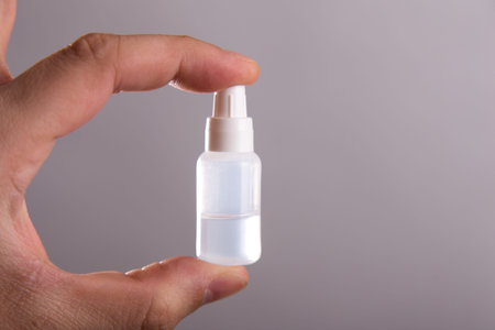 A small tube with a colorless liquid in a hand on a gray background