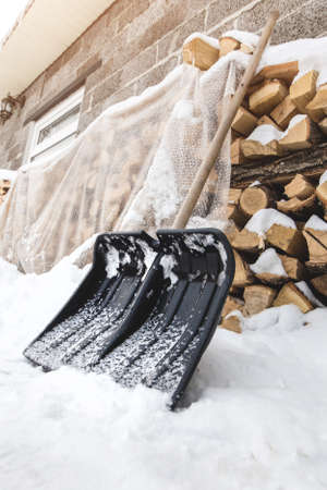 A shovel for cleaning snow near a pile of firewood in the backyard by a winter dayの写真素材