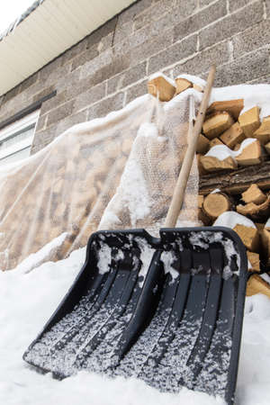 A shovel for cleaning snow near a pile of firewood in the backyard by a winter dayの写真素材