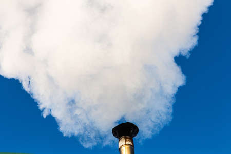 Smoke comes from the chimney of the house against the blue sky. The pipe on the roof. Chimney. Country house.の写真素材