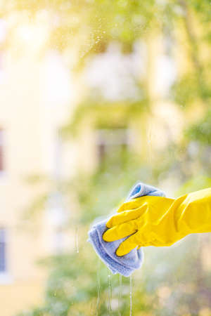 A female hand in bright yellow rubber gloves washes. cleaning the window with a soft rag. Nice view from the windowの写真素材