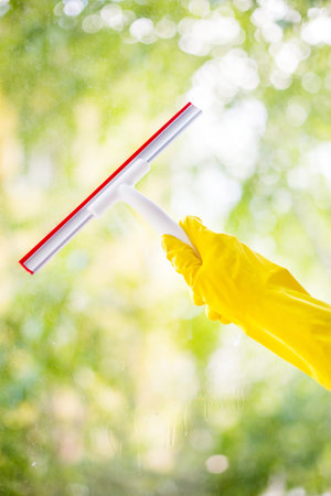 hand cleaning glass window pane with detergent and rubber aluminum wiper. A female hands in bright yellow gloves washes the windowsの写真素材