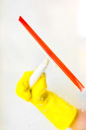 hand cleaning glass window pane with detergent and rubber aluminum wiper. A female hands in bright yellow gloves washes the windowsの写真素材