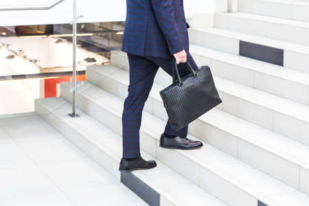 A businessman in a suit with a briefcase climbs the stairs in the business center. The concept of career ladder and successの写真素材