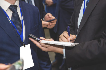 A man in a jacket with a dictaphone interviews a businessman and writes to a notebook. Close-up