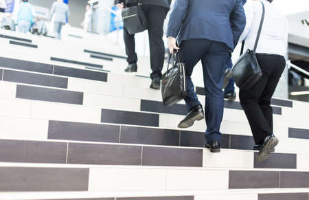 Several businessmen in suits with briefcases go up the stairs in the business center. The concept of career ladder and successの写真素材