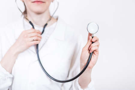 Young smiling woman brunette doctor in glasses and medical white coat, working stethoscope close-up on a white backgroundの写真素材