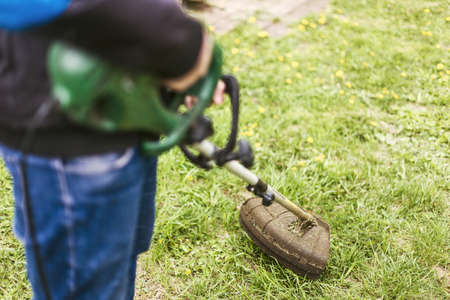 Men's hands holding a lawn mower and cut the grass on the site.の写真素材