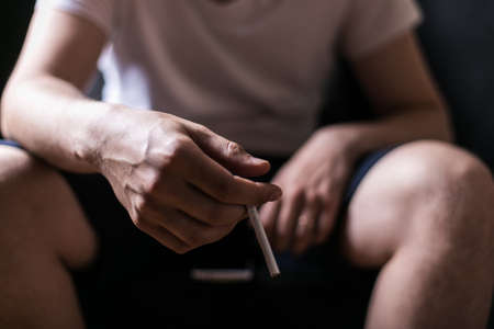 Stop smoking. Dependence on cigarettes, nicotine addiction. portrait of a man on a black background with a cigarette in his handの写真素材